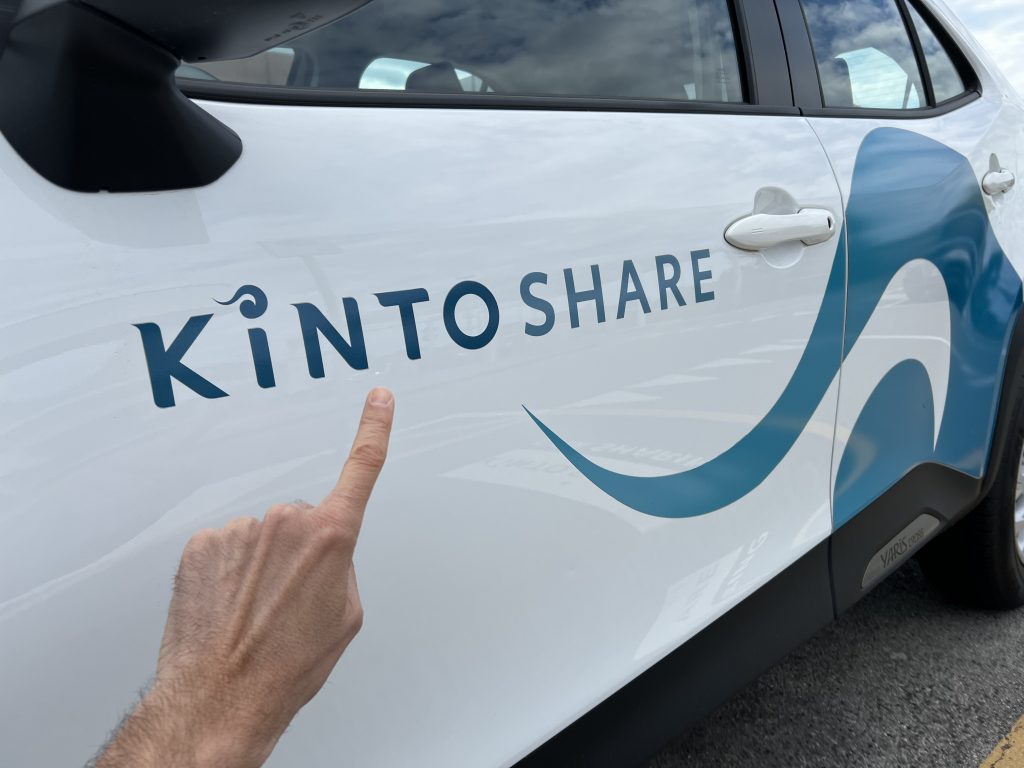 Mano indica scritta Kinto share su auto in car-sharing